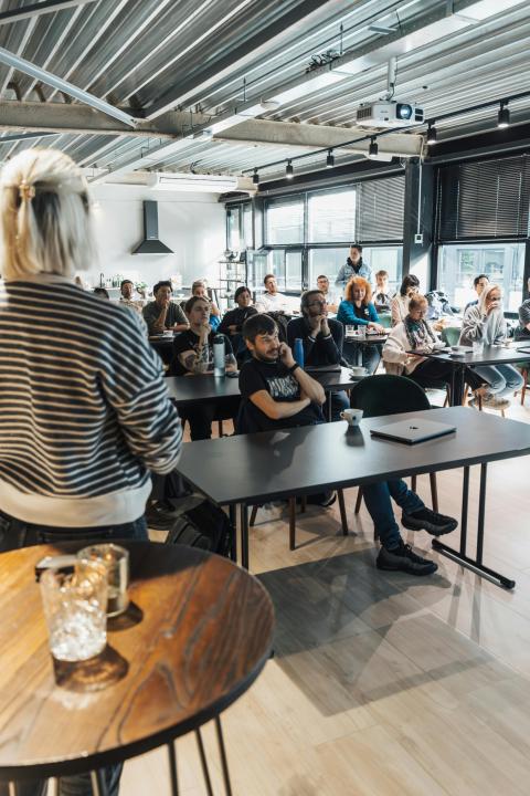 Woman standing and presenting in front of full audience seated in a classroom style setting